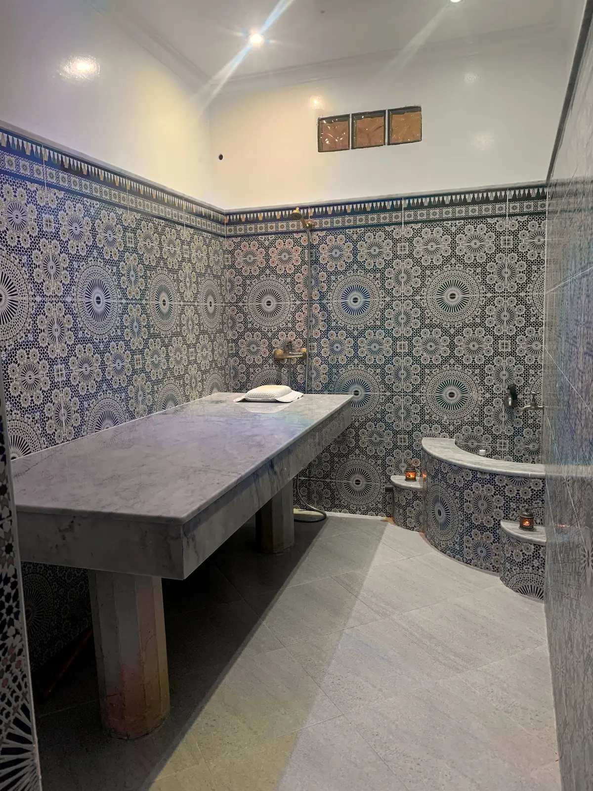 Le hammam privé : murs en zellige bleu et vert, banc de marbre, vasque et robinetterie en laiton