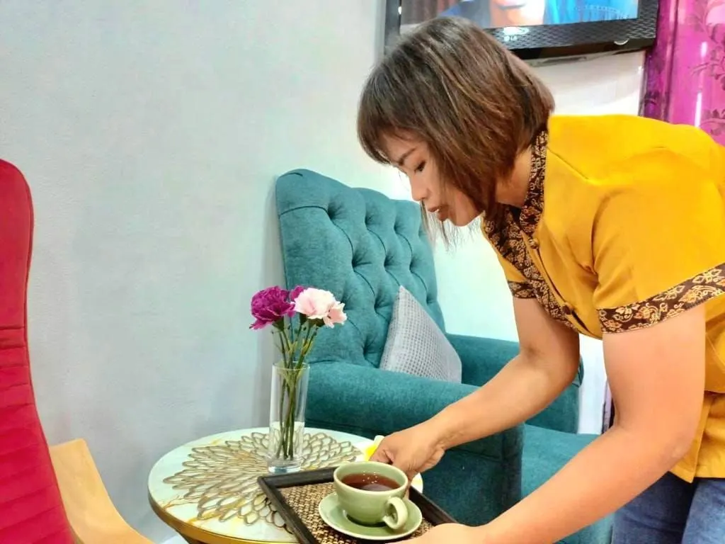 Une masseuse sert le thé sur la table dorée, près d’un fauteuil bleu canard