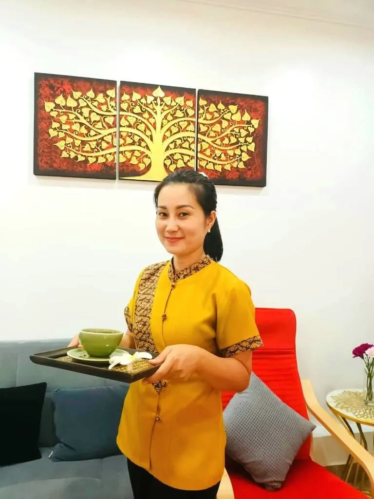 Une masseuse en tunique safran apporte le plateau du thé devant un triptyque doré de l’arbre de la Bodhi
