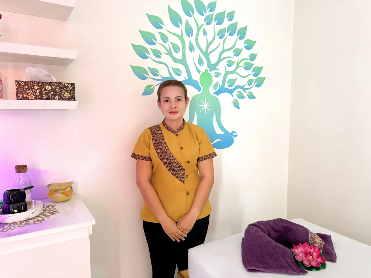 Une thérapeute en tunique safran devant le motif d’arbre de vie au mur d’une salle de soin