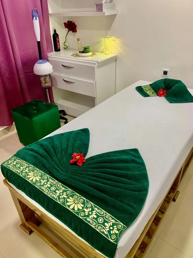 Lit de massage, serviette vert bouteille à bordure dorée pliée en éventail, fleur rouge