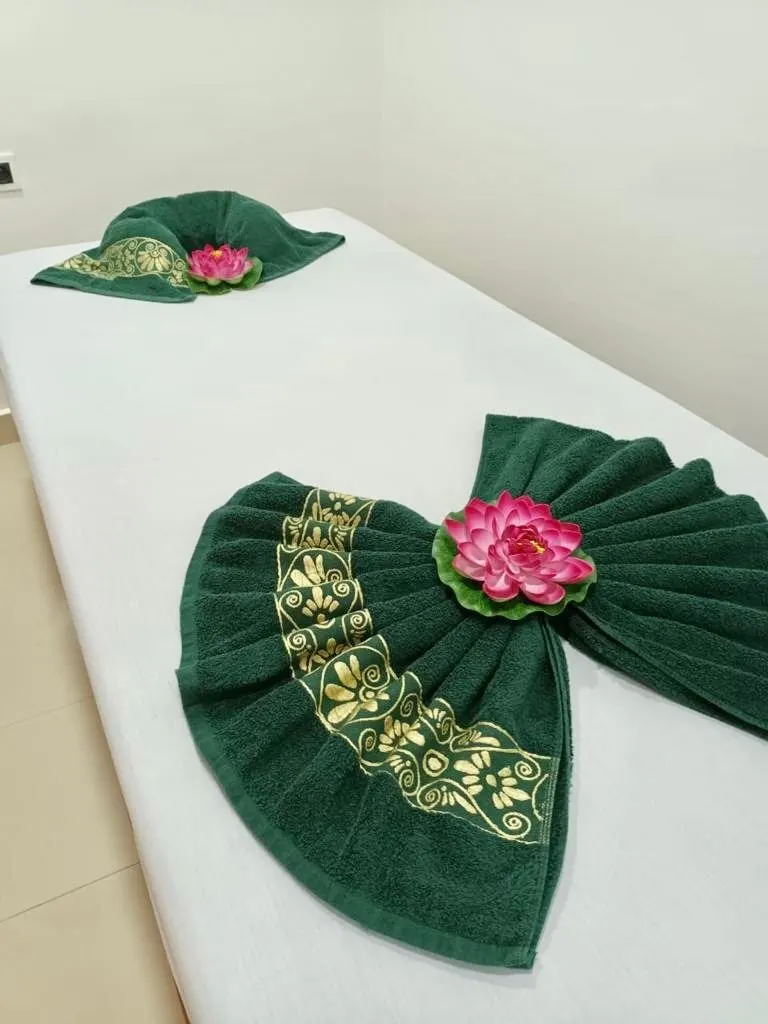 Serviette vert bouteille à bordure dorée pliée en éventail, lotus rose