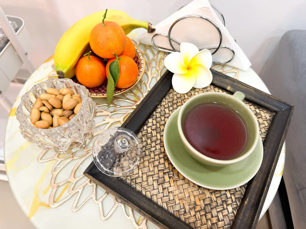 Le plateau du thé : thé thaï dans une tasse céladon, mandarines, banane, cacahuètes dans une coupe en cristal et une fleur de frangipanier